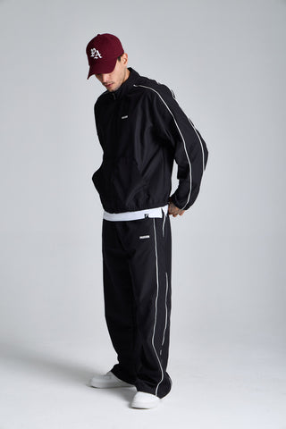 Erkek model üzerinde siyah Piping Track Jacket ve Jogger takımı, açılı tam boy görünüm