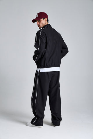 Erkek model üzerinde siyah Piping Track Jacket ve Jogger takımı, yandan tam boy görünüm