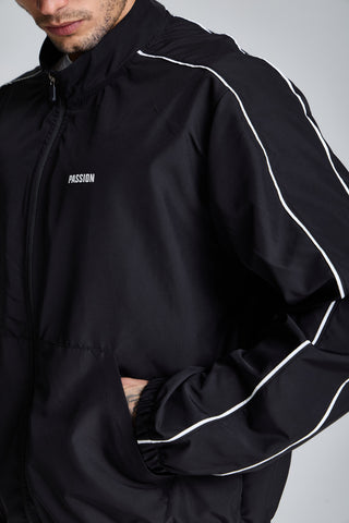 Erkek model üzerinde siyah Piping Track Jacket, göğüsteki PASSION logosu, biye ve cep yakın çekim