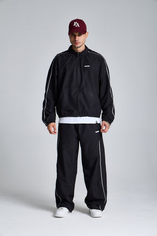 Erkek model üzerinde siyah Piping Track Jogger ve Jacket takımı, düz duruşta tam boy görünüm